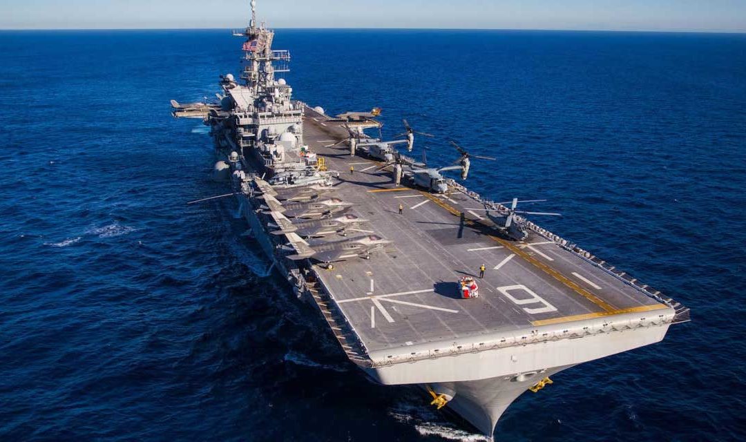 The USS America, a large air craft carrier in the ocean with several aircraft on it