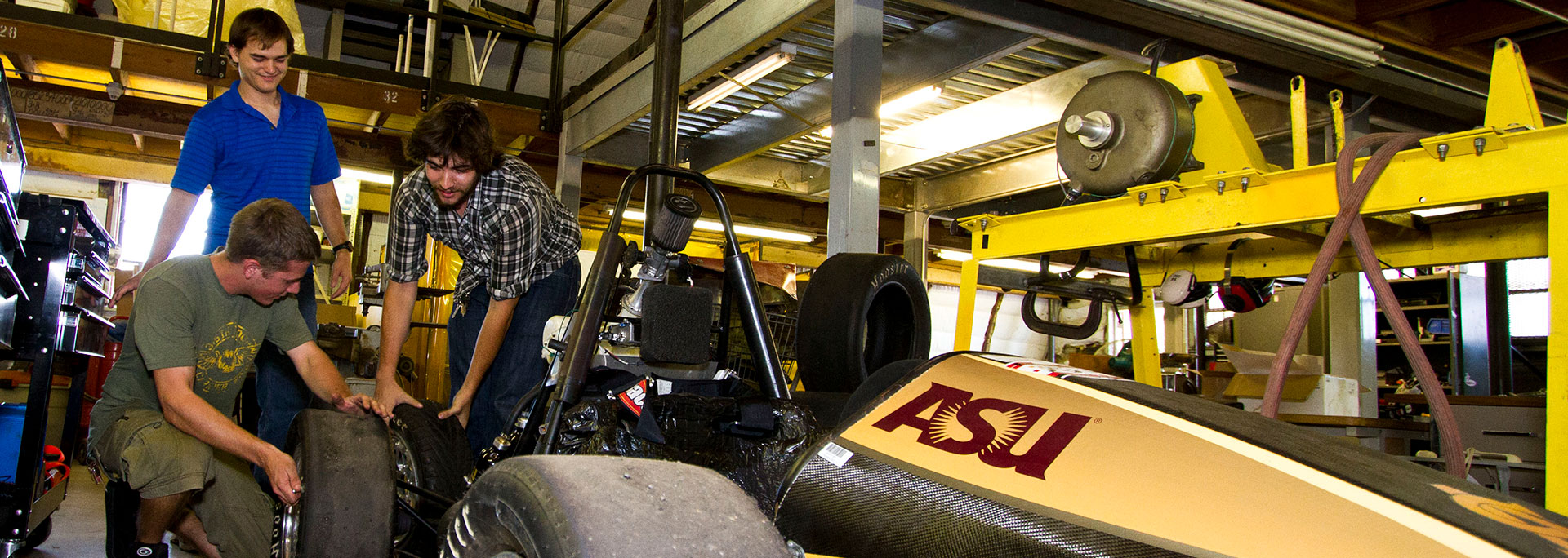 Three male students switching out a tire on a race car.