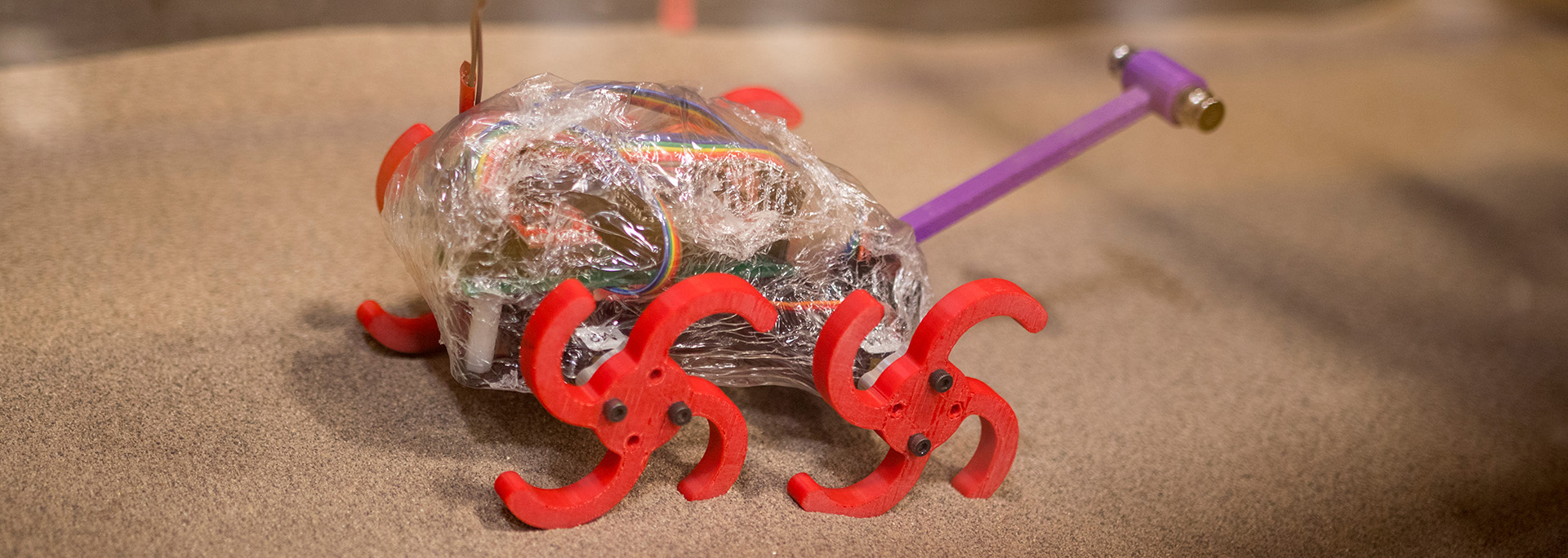 A robotic system with red wheels on sand.