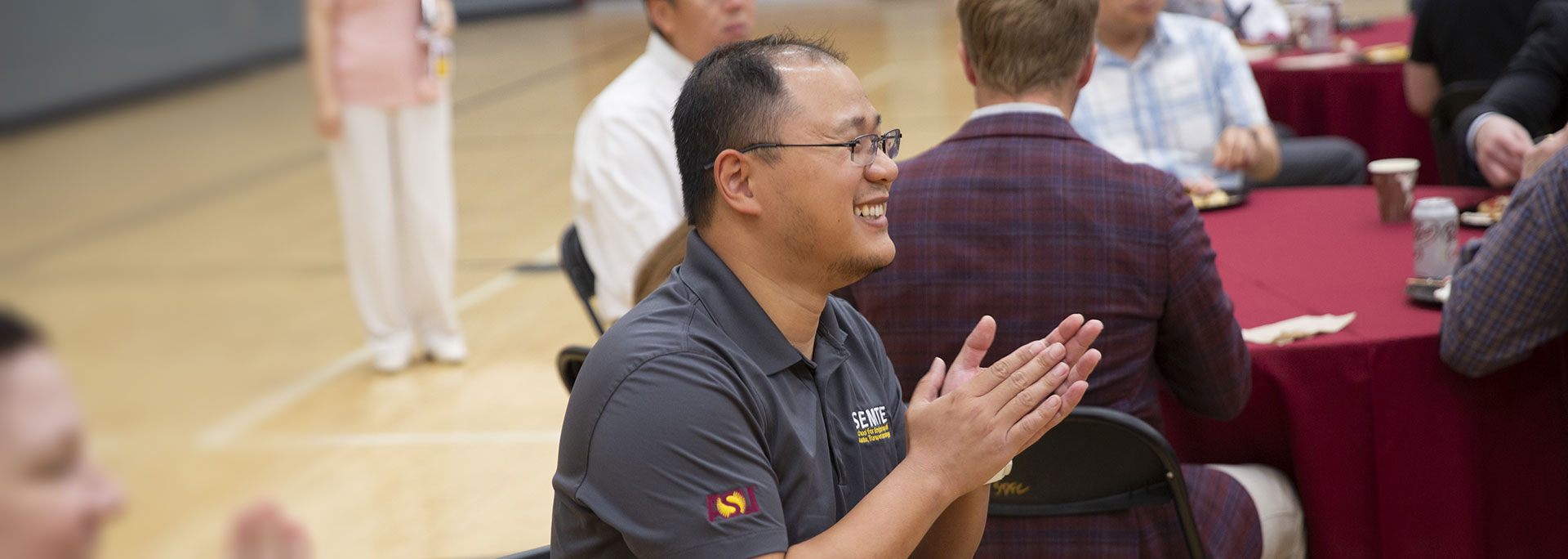 Man sitting at a table during an event and clapping.